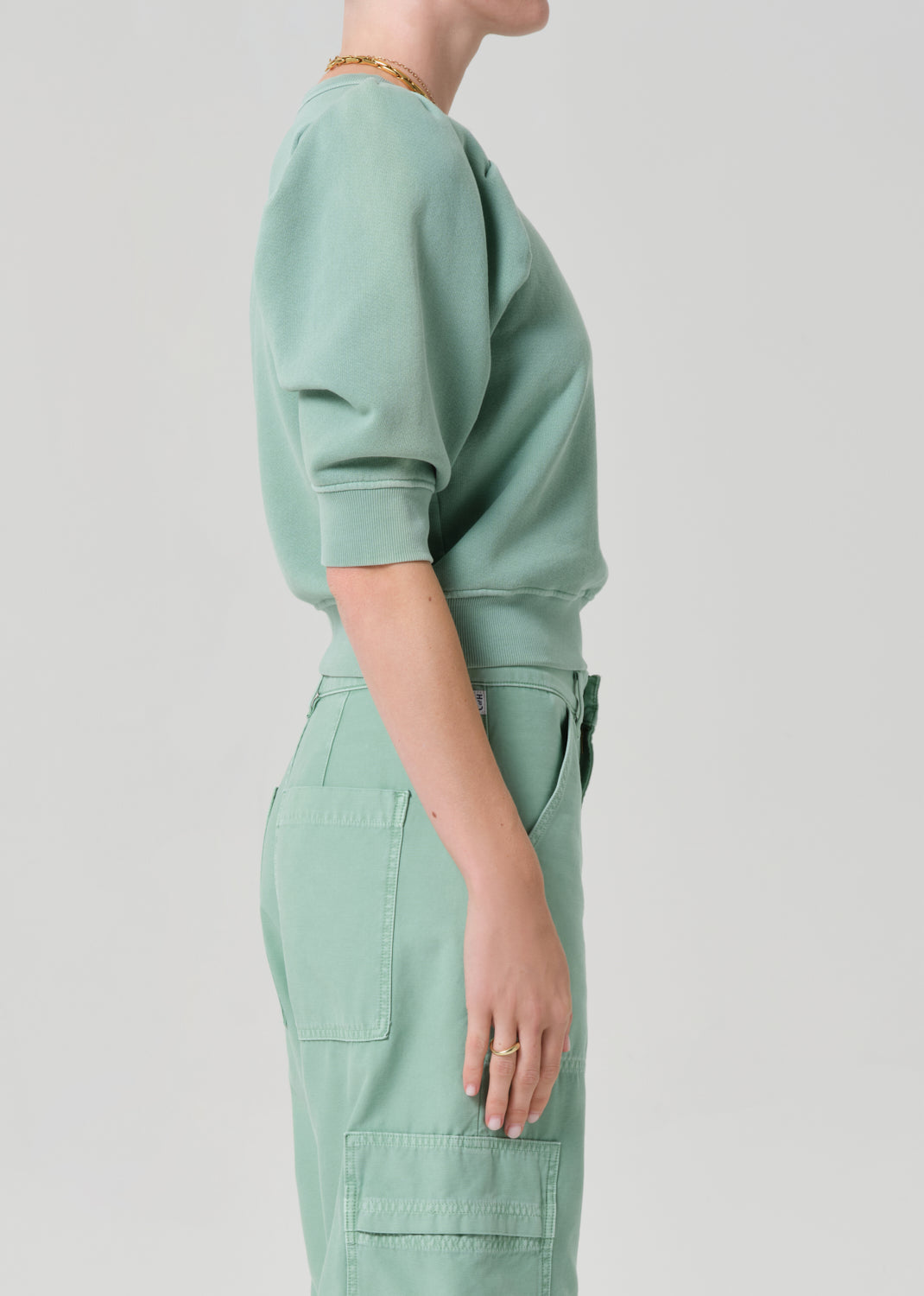 Person wearing a matching green sweater and cargo pants on a light gray background