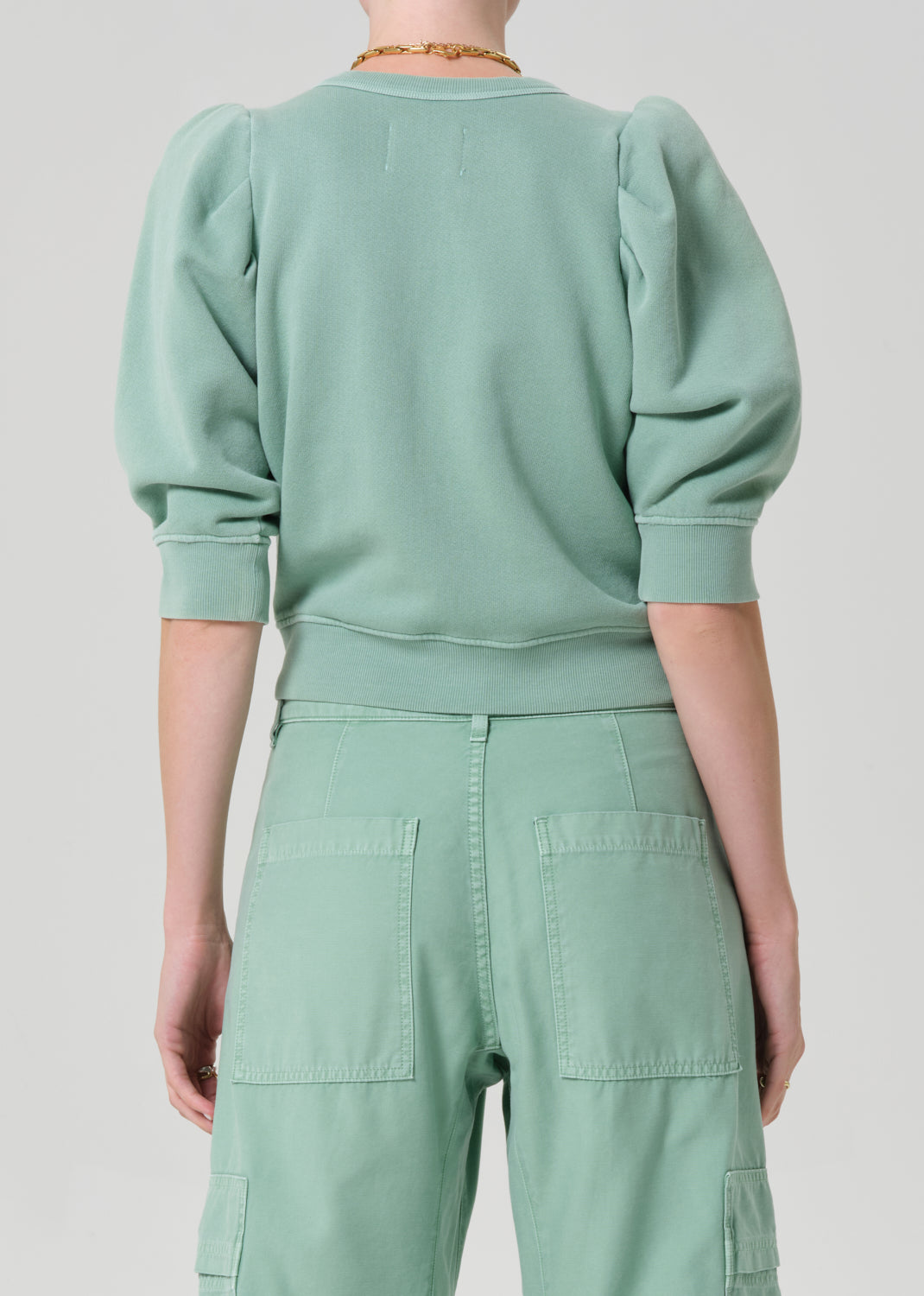 Person wearing a matching green sweater and cargo pants on a light gray background