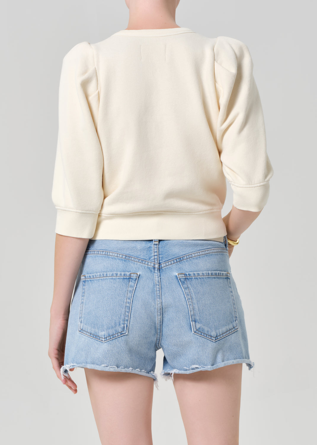 Person wearing a cream sweater and light blue denim shorts on a gray background