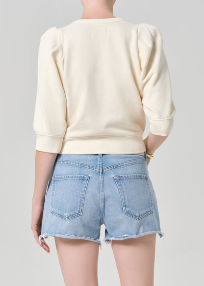 Person wearing a cream sweater and light blue denim shorts on a gray background