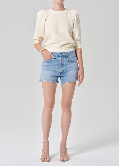 Person wearing a cream sweater and light blue denim shorts on a gray background