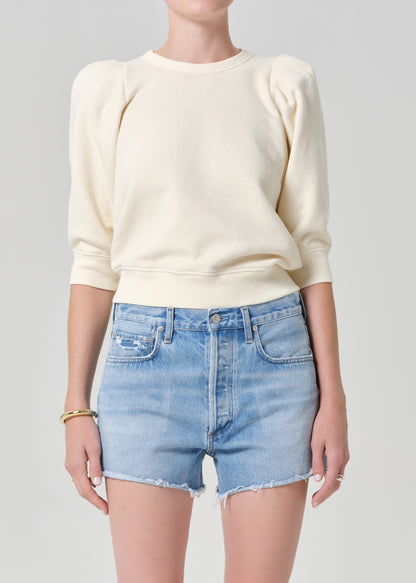 Person wearing a cream sweater and light blue denim shorts on a gray background