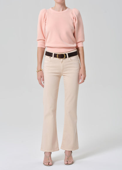 Person wearing a pink sweater and light pink pants with a belt on a gray background