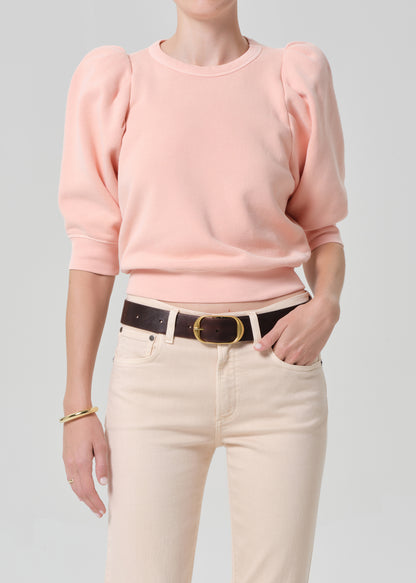 Person wearing a pink sweater and light pink pants with a belt on a gray background