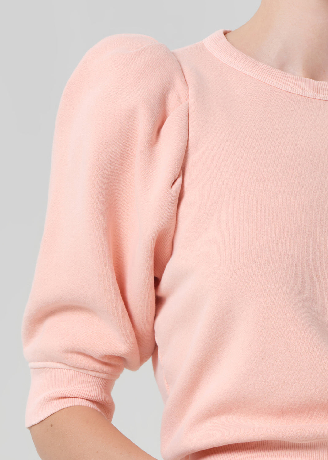 Person wearing a pink sweater and light pink pants with a belt on a gray background