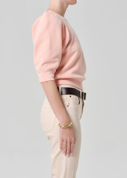 Person wearing a pink sweater and light pink pants with a belt on a gray background