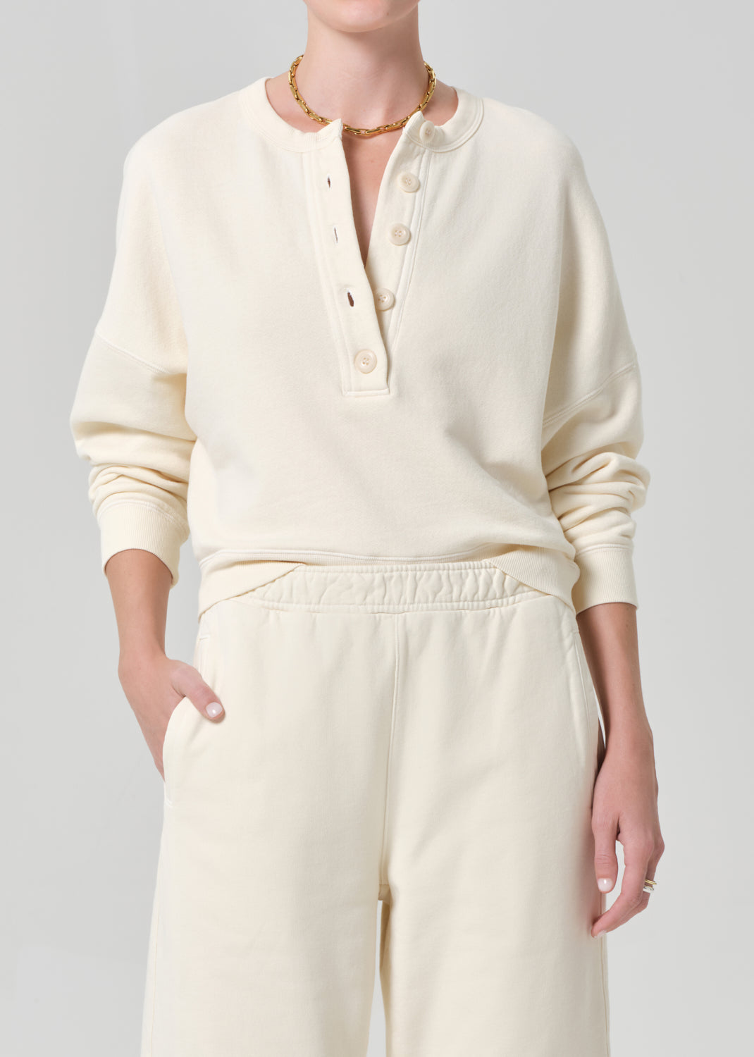 Person wearing a cream-colored sweatshirt and sweatpant on a gray background