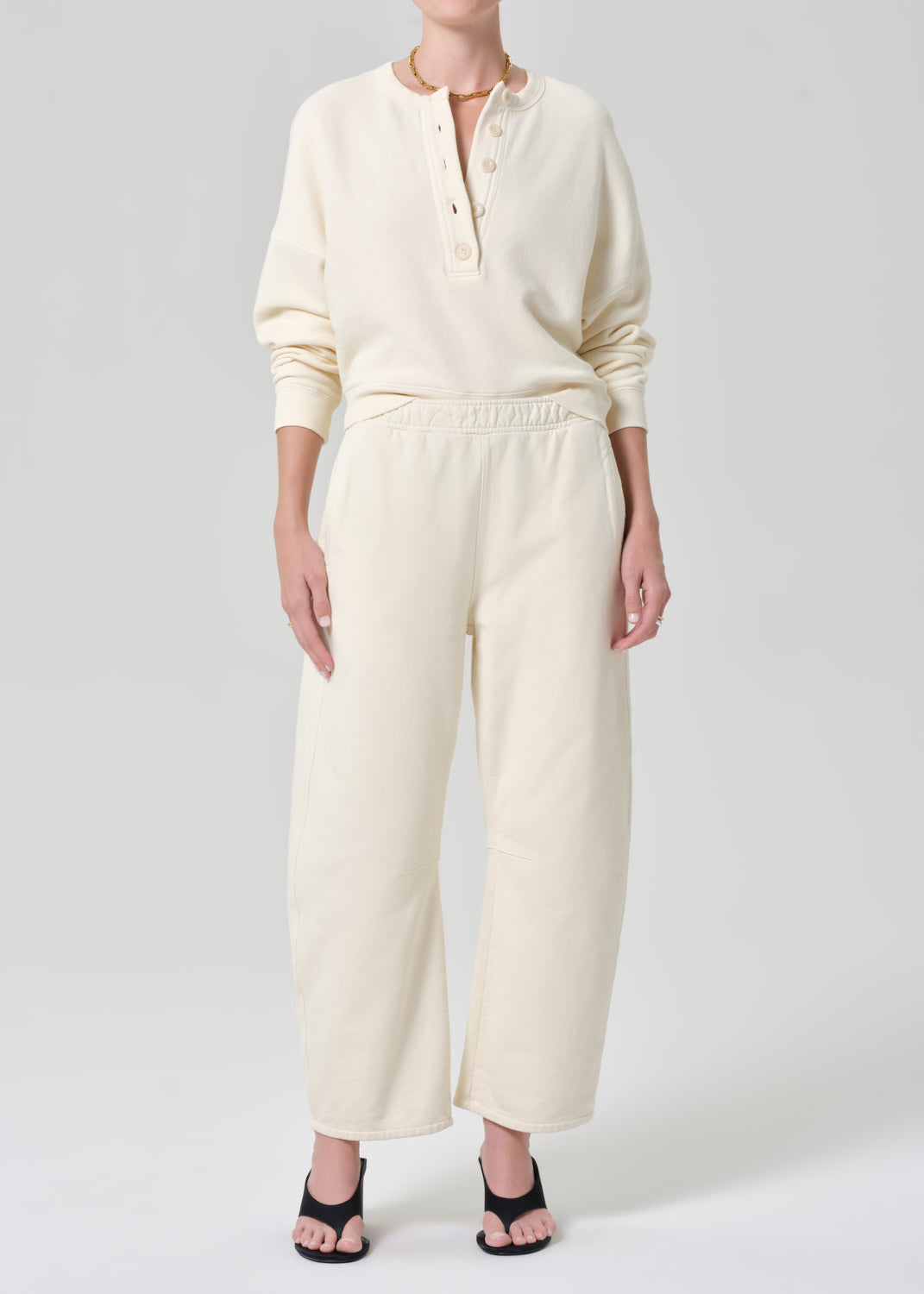 Person wearing a cream-colored sweatshirt and sweatpant on a gray background