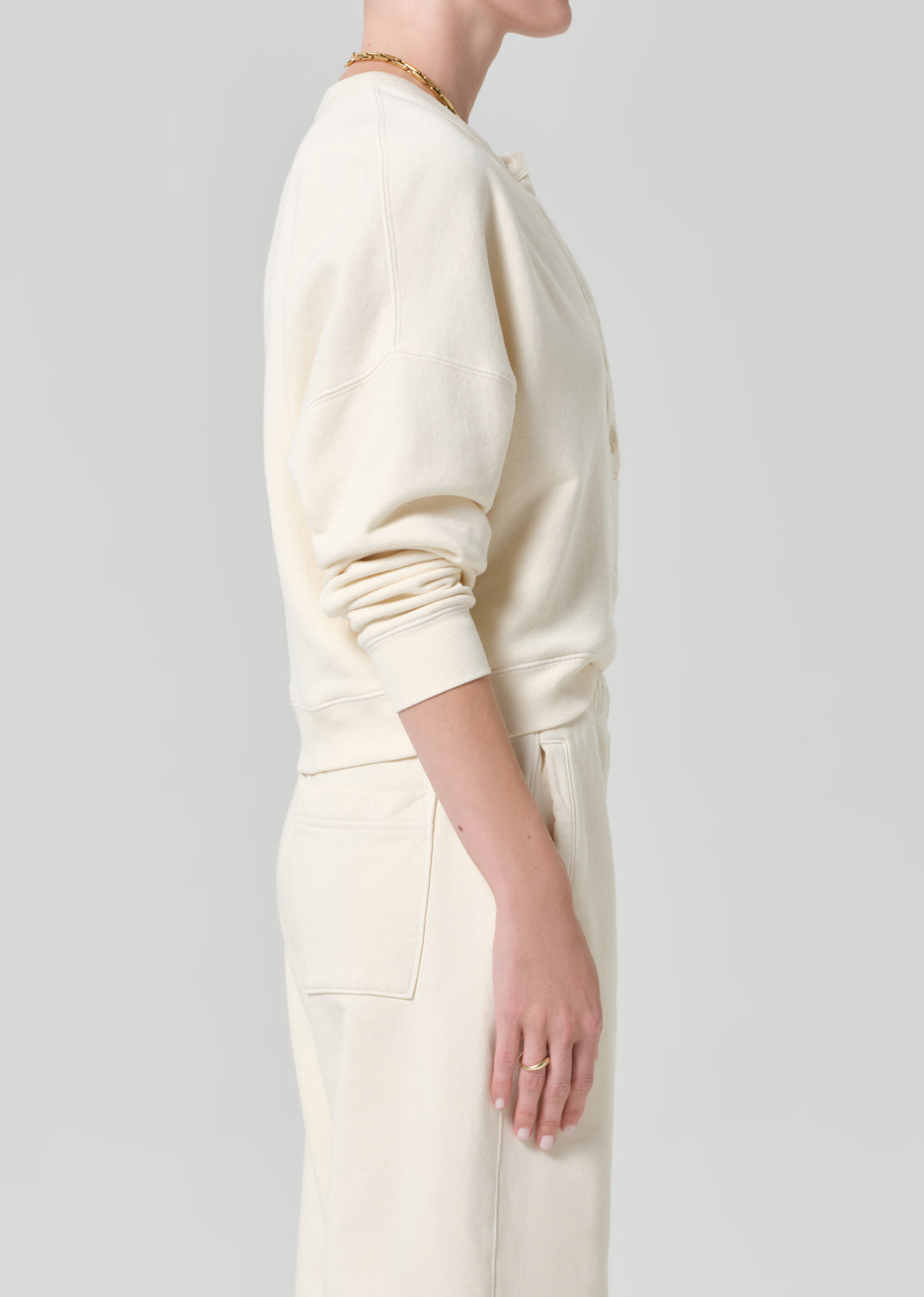 Person wearing a cream-colored sweatshirt and sweatpant on a gray background