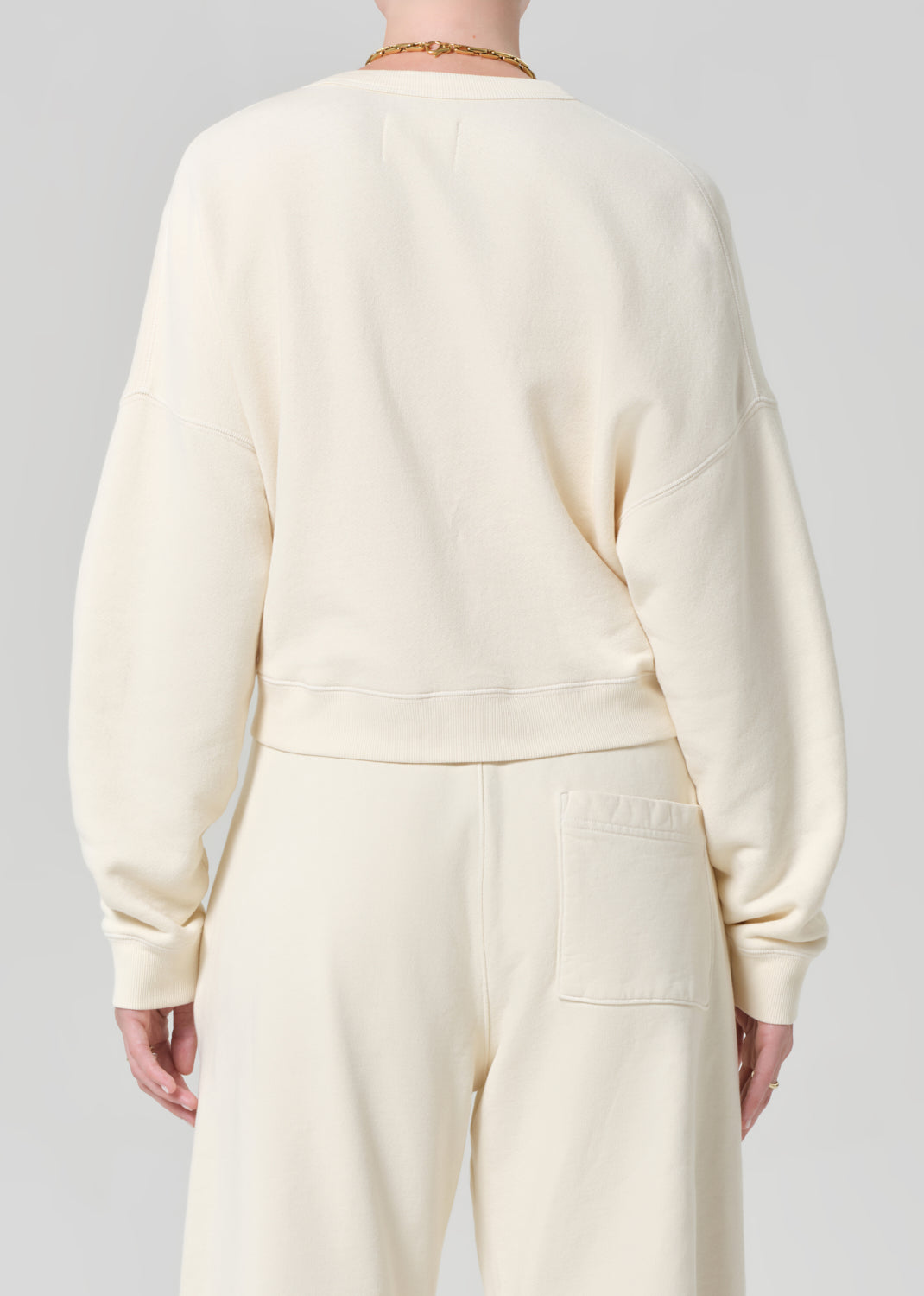 Person wearing a cream-colored sweatshirt and sweatpant on a gray background