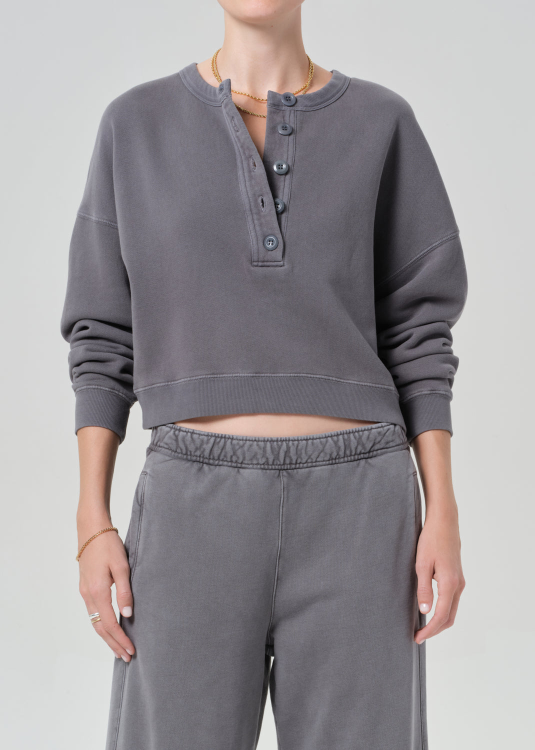 Person wearing a gray cropped sweatshirt and pants on a plain background