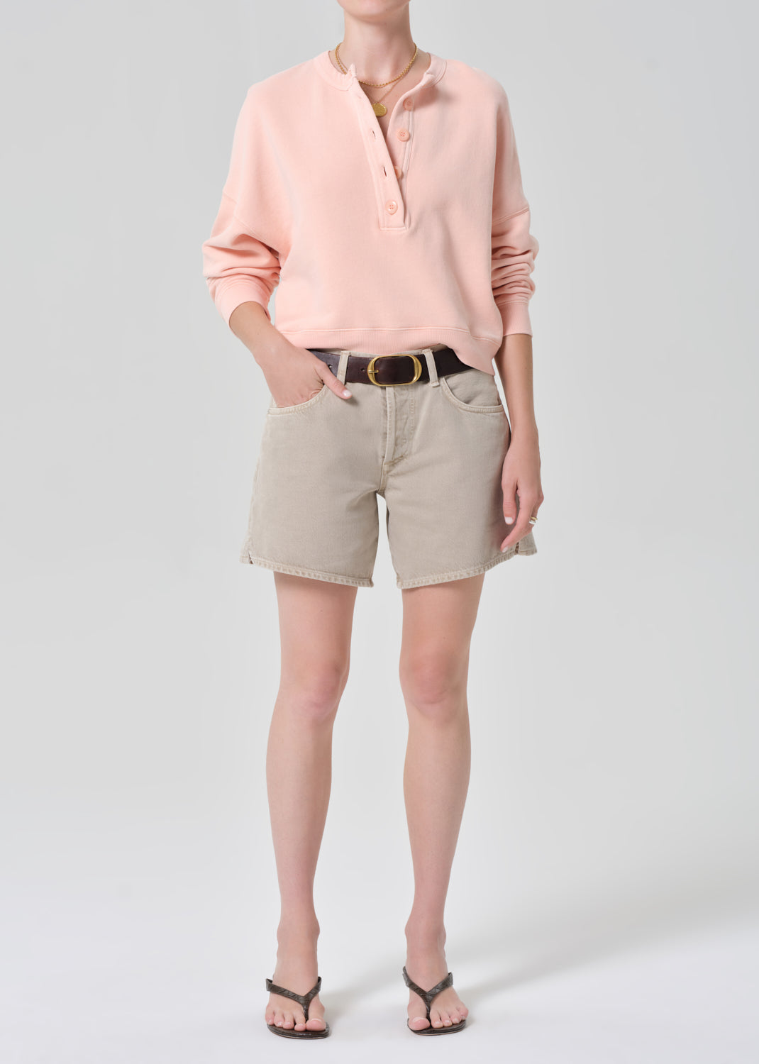 Person wearing a pink sweatshirt and beige shorts on a gray background