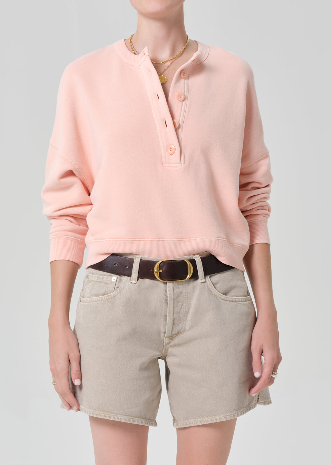 Person wearing a pink sweatshirt and beige shorts on a gray background