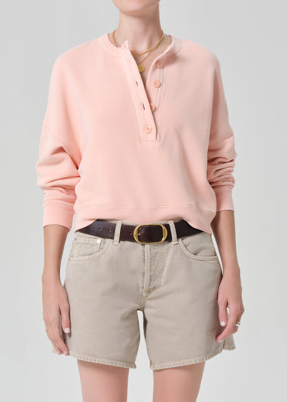 Person wearing a pink sweatshirt and beige shorts on a gray background