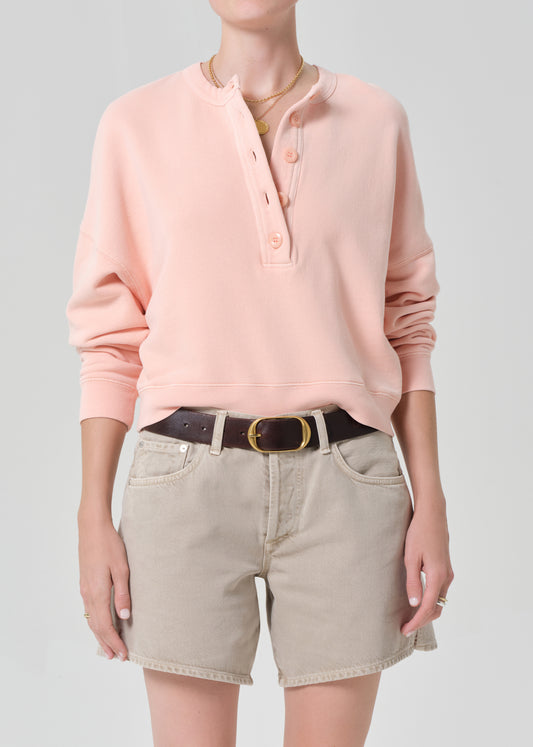 Person wearing a pink sweatshirt and beige shorts on a gray background