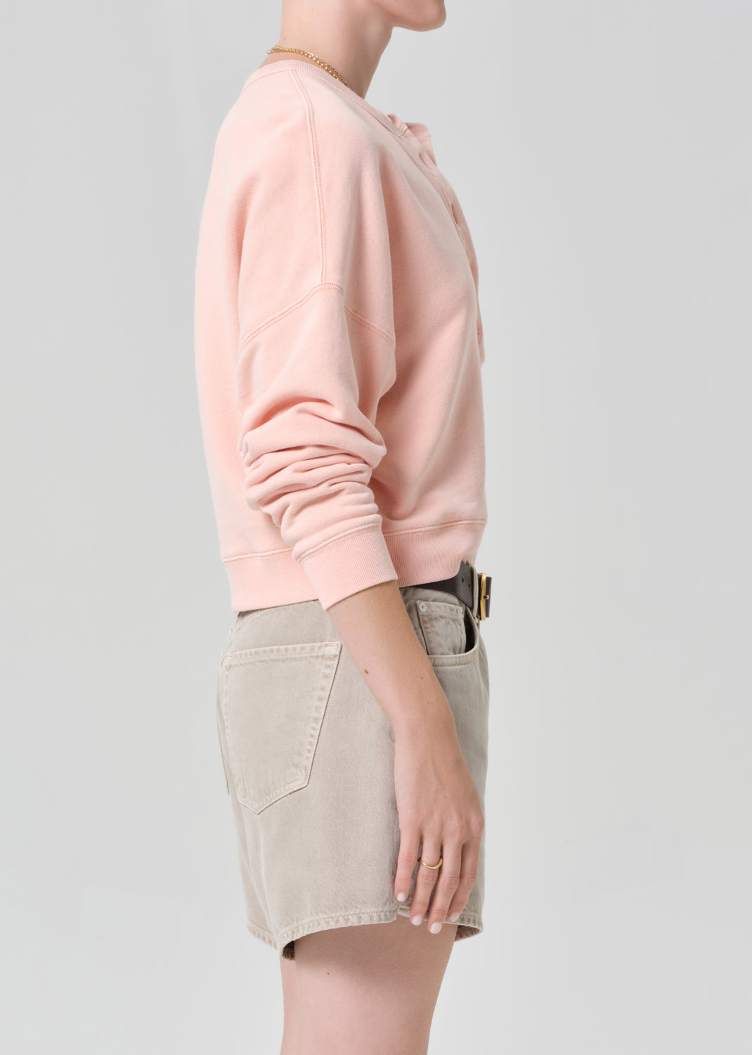 Person wearing a pink sweatshirt and beige shorts on a gray background