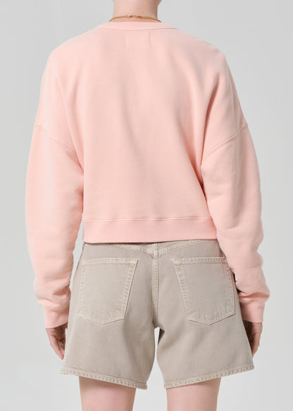 Person wearing a pink sweatshirt and beige shorts on a gray background