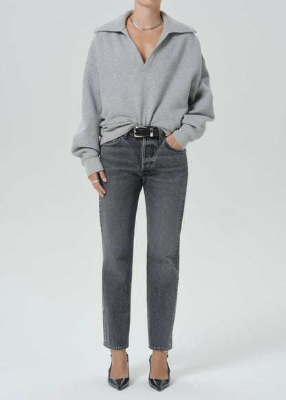 A model wearing a light grey oversized knit sweater with a collar, tucked into dark grey straight-leg jeans with a black belt, paired with black pointed-toe heels, against a grey background.