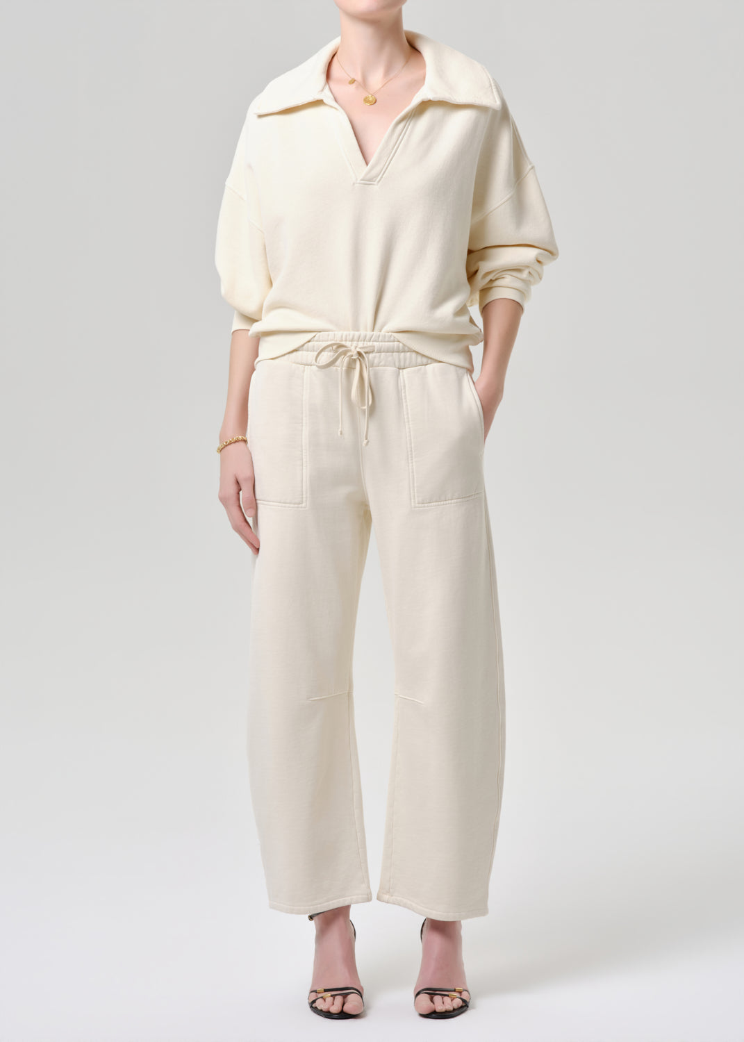 Person wearing a cream-colored outfit with a matching top and pants on a grey background.