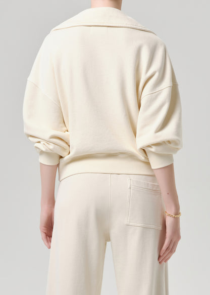 A person shown from the back wearing a cream-colored oversized sweatshirt and matching cream pants against a grey background.