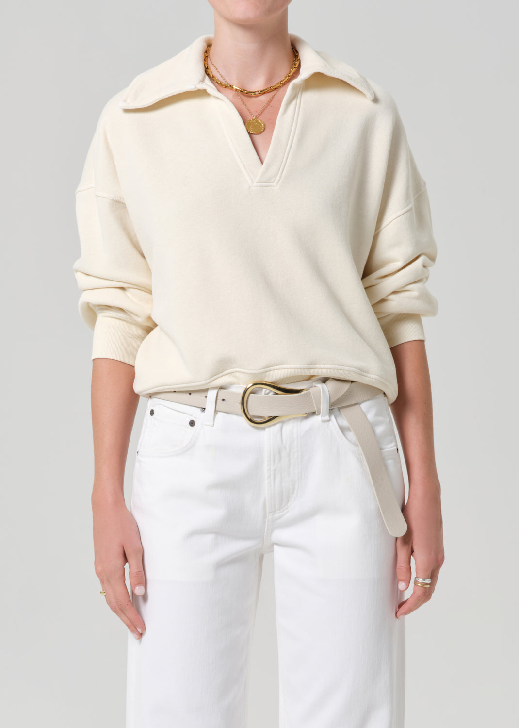 Person wearing a cream-colored sweatshirt and white jeans on a plain background