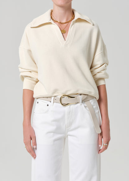 Person wearing a cream-colored sweatshirt and white jeans on a plain background