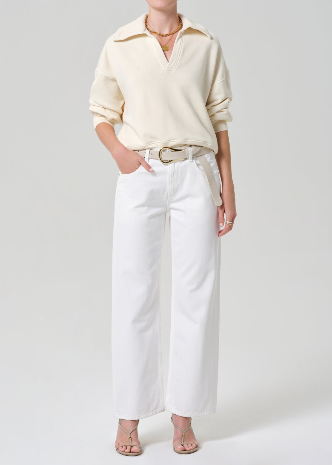 Person wearing a cream-colored sweatshirt and white jeans on a plain background