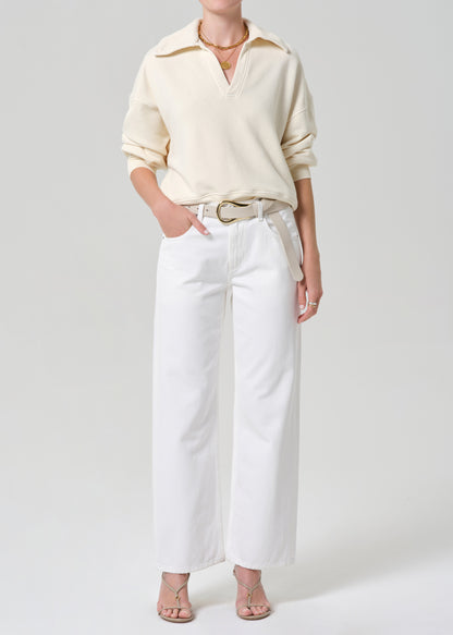 Person wearing a cream-colored sweatshirt and white jeans on a plain background