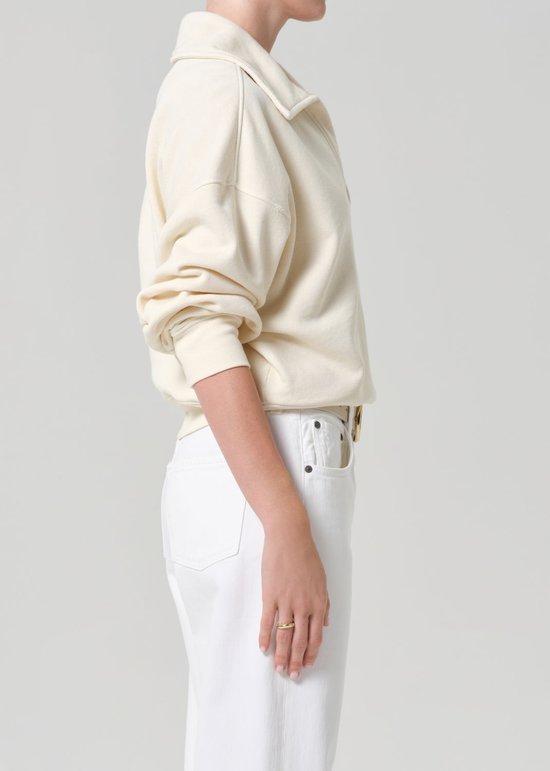 Person wearing a cream-colored sweatshirt and white jeans on a plain background