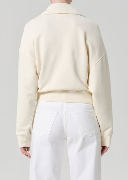 Person wearing a cream-colored sweatshirt and white jeans on a plain background