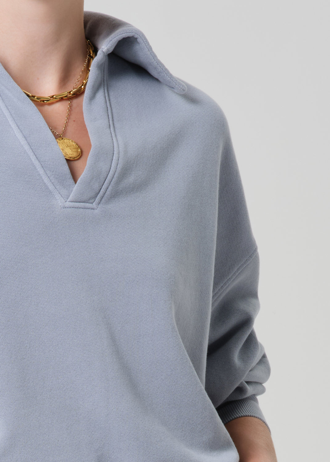 Gray sweater with a V-neck and gold necklace on a light gray background