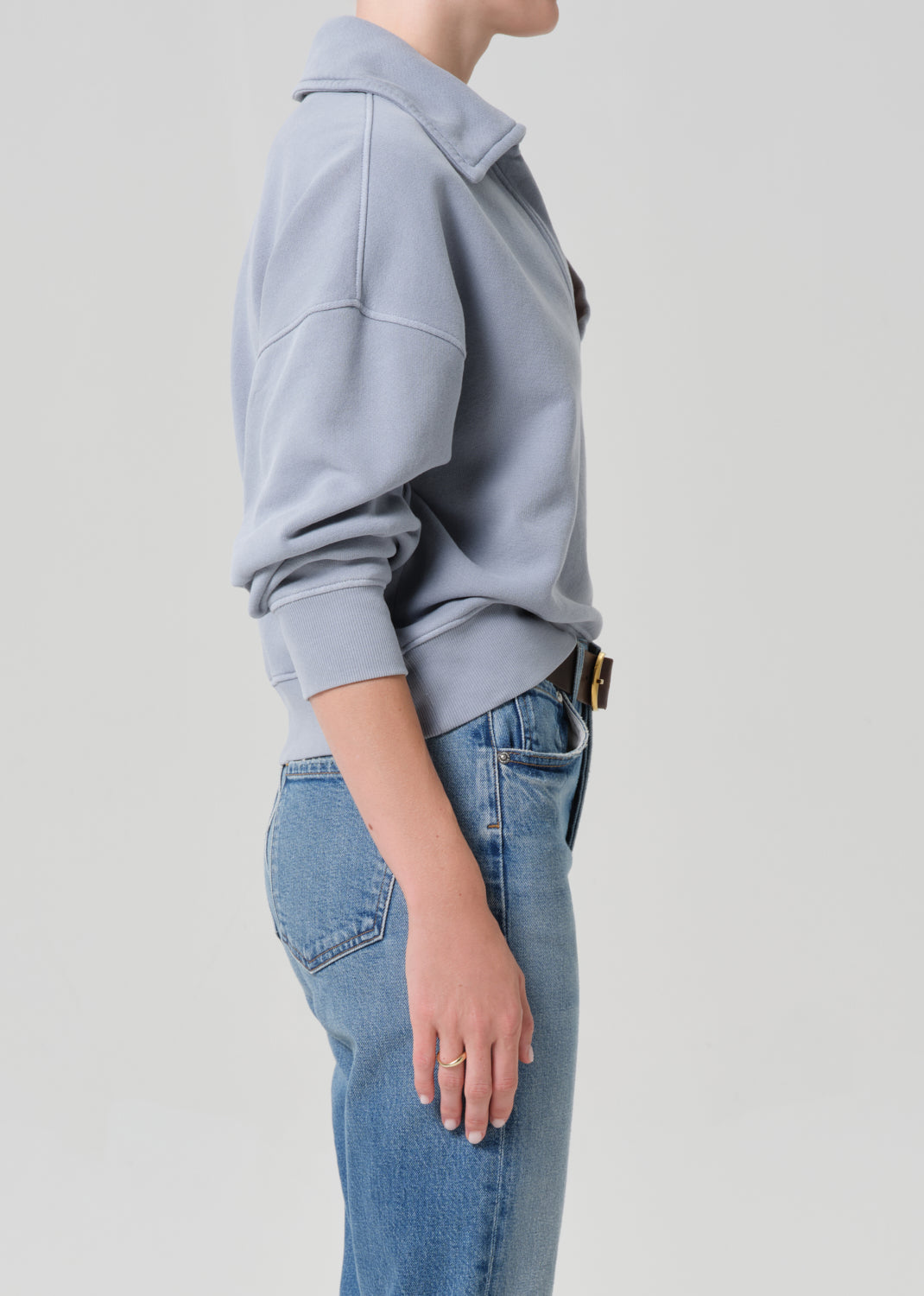 Person wearing a light gray sweatshirt and blue jeans on a plain background
