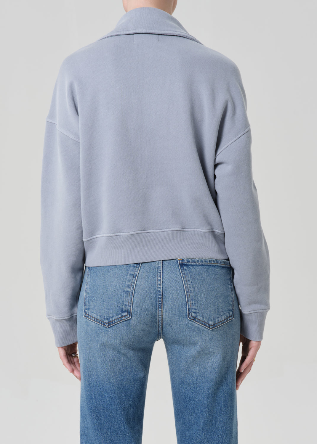 Person wearing a light blue sweatshirt and jeans on a plain background