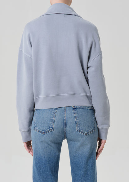 Person wearing a light blue sweatshirt and jeans on a plain background