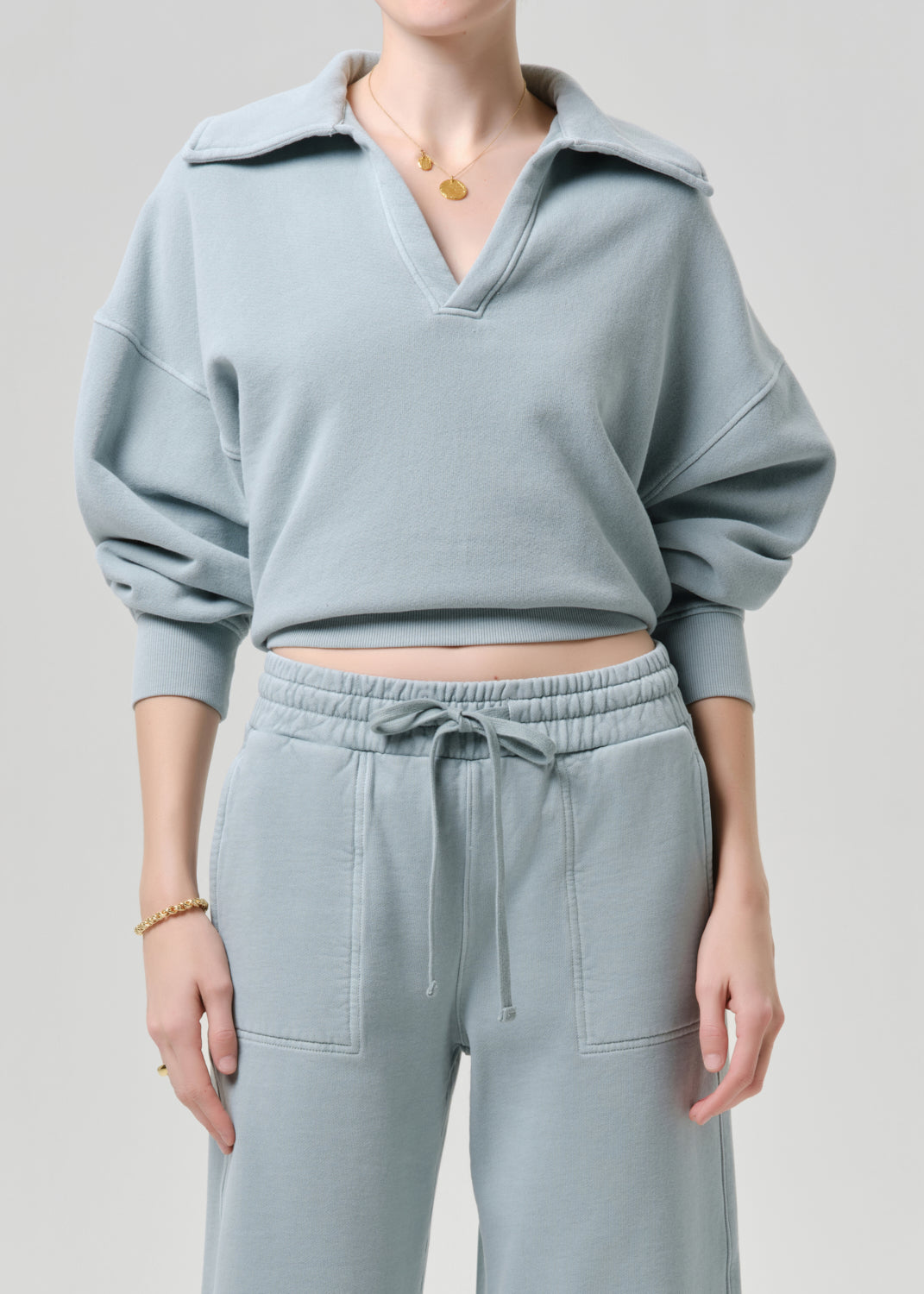 Person wearing a light blue pullover and pants set on a grey background