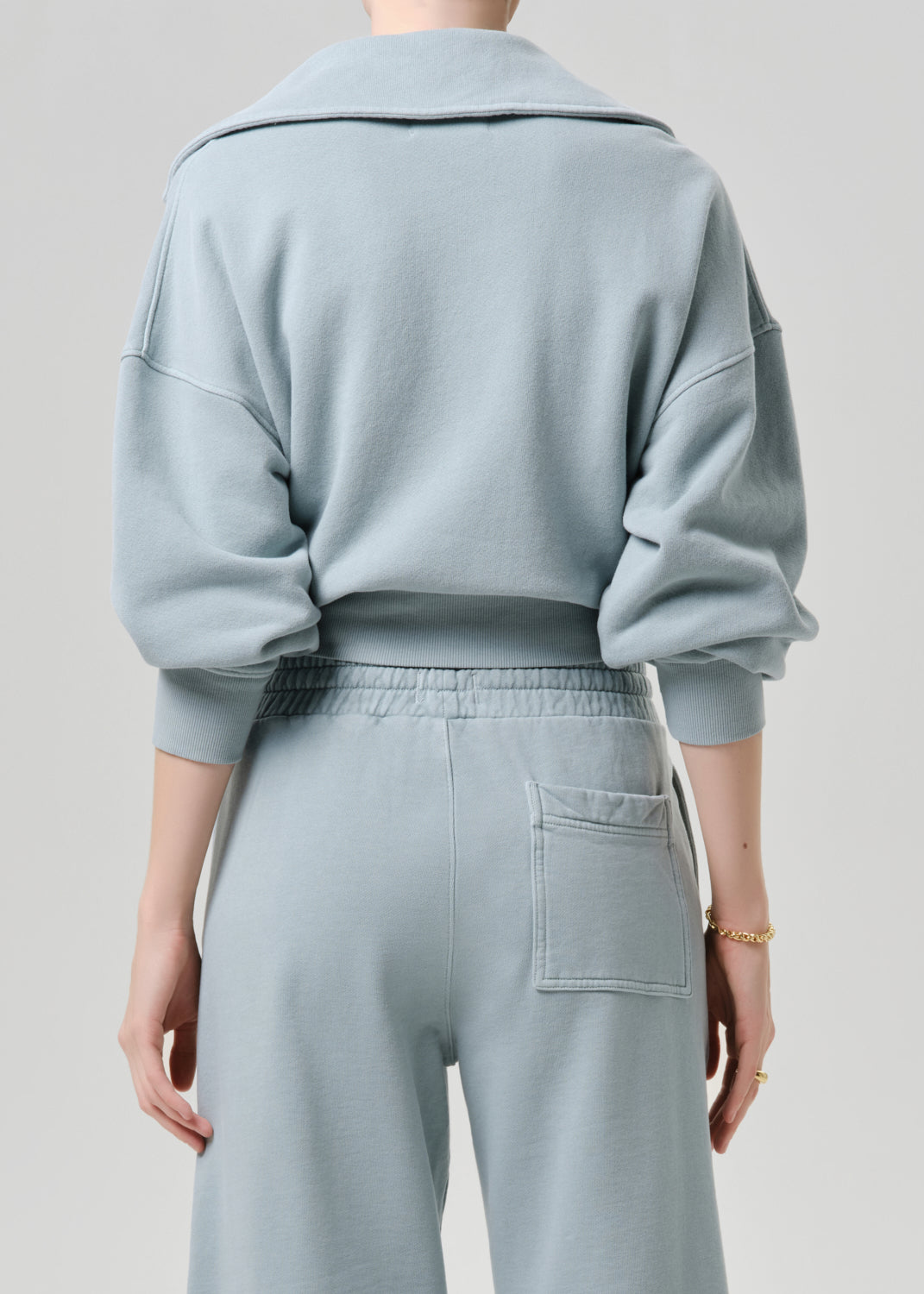Person wearing a light blue outfit with a matching jacket and pants on a grey background