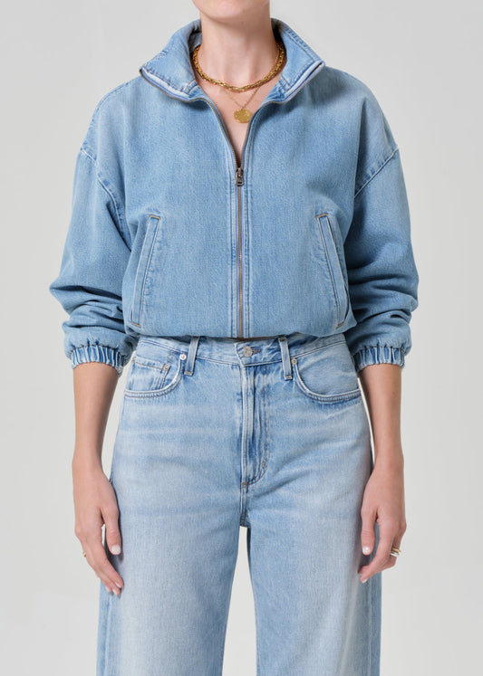 Person wearing a light blue denim jacket and jeans on a plain background