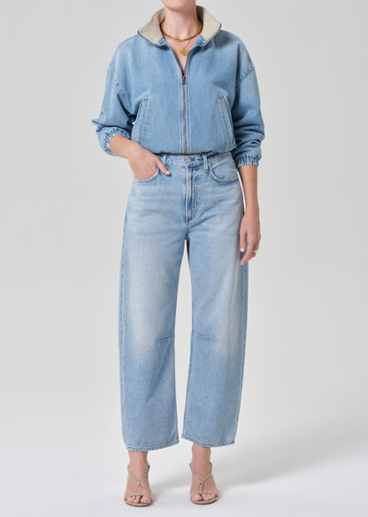 Person wearing a light blue denim jacket and jeans on a grey background