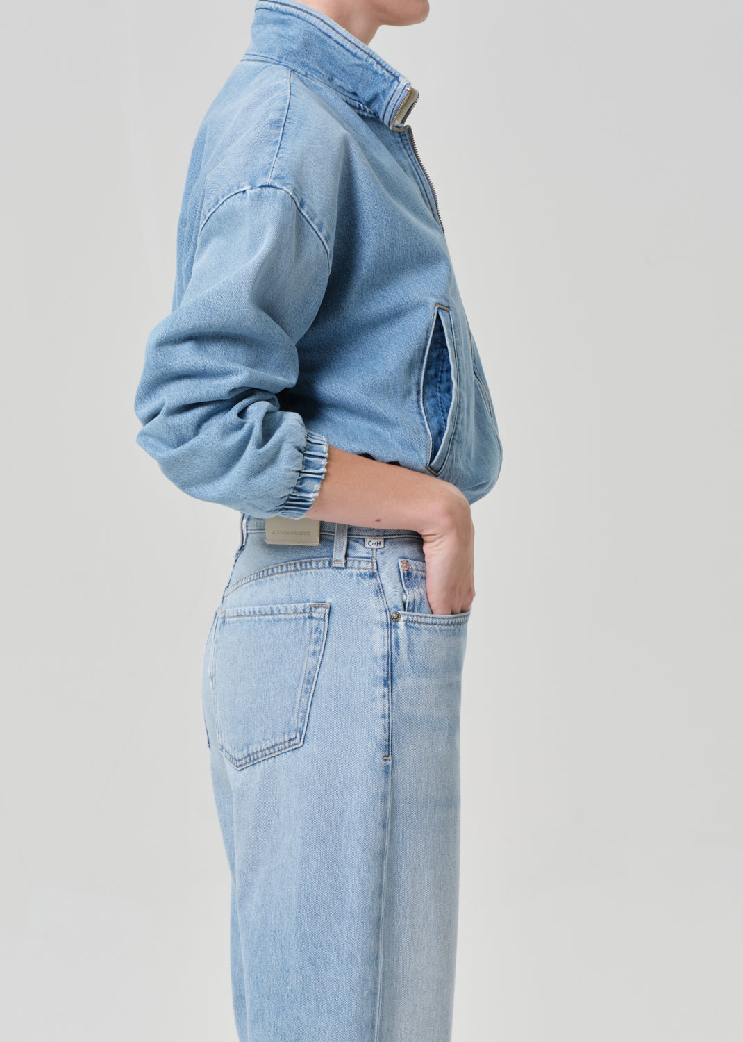 Person wearing a light blue denim jacket and jeans on a plain background