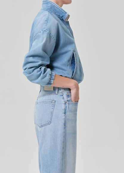 Person wearing a light blue denim jacket and jeans on a plain background