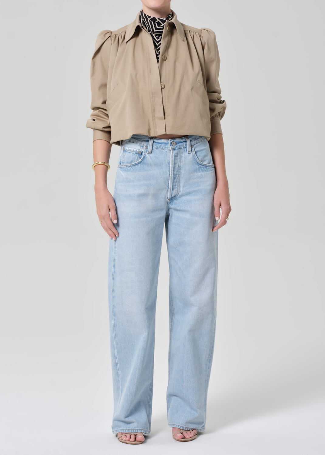 Person wearing a beige jacket with puffed sleeves and light blue jeans on a plain background