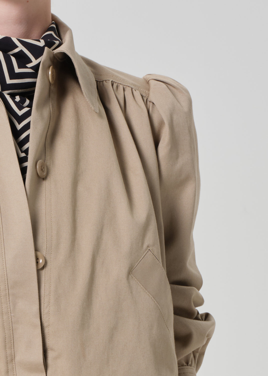 Person wearing a beige jacket with puffed sleeves on a plain background