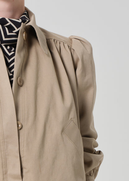 Person wearing a beige jacket with puffed sleeves on a plain background