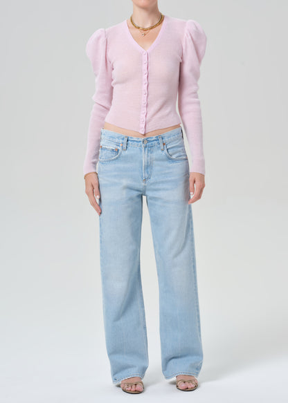 Person wearing a pink cardigan and light blue jeans on a grey background