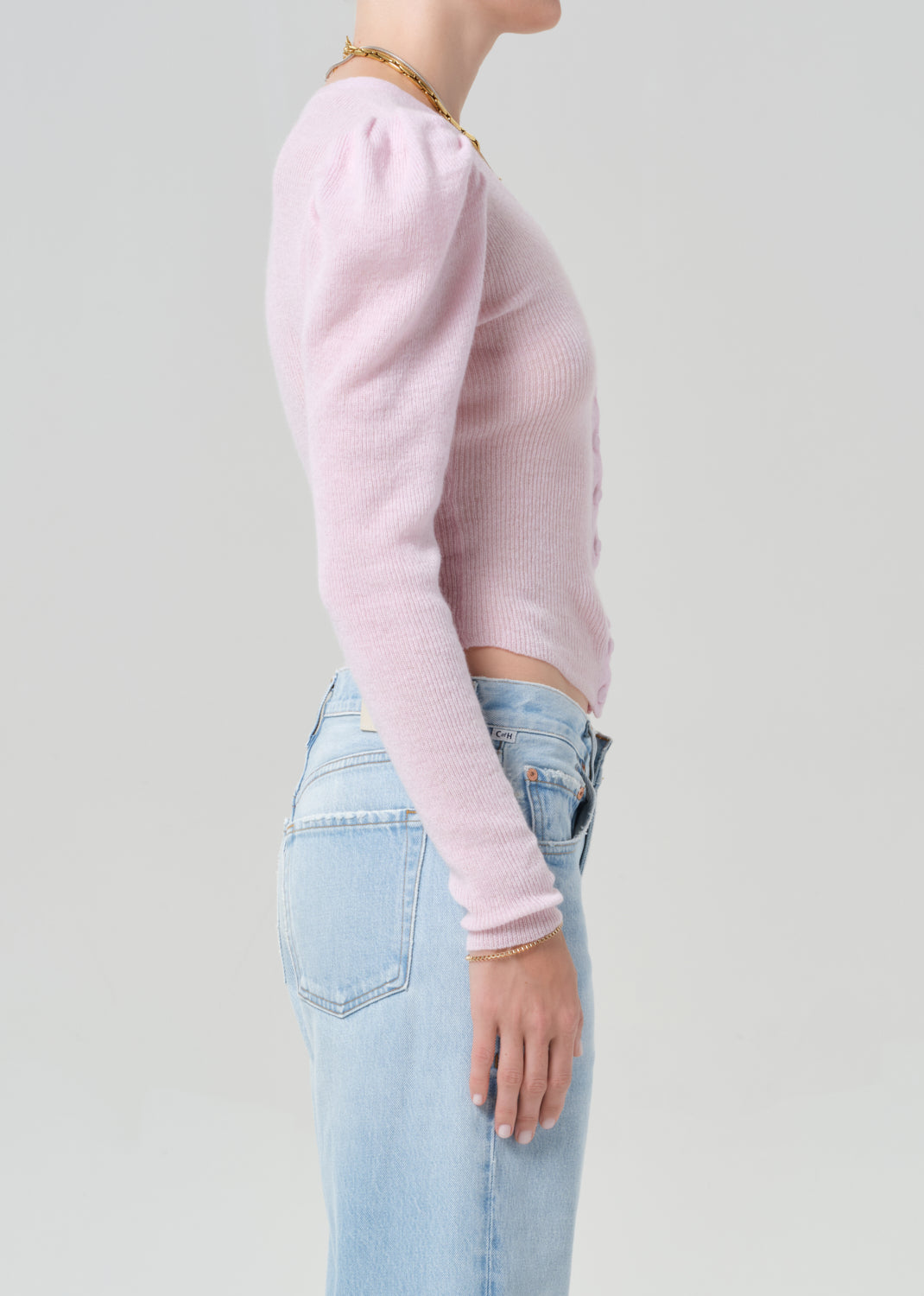 Person wearing a light pink long-sleeve top and light blue jeans on a plain background