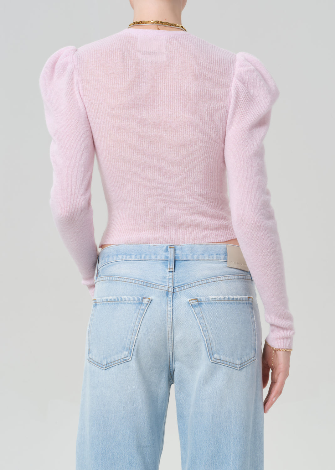 Person wearing a pink sweater with puffed sleeves and light blue jeans on a plain background