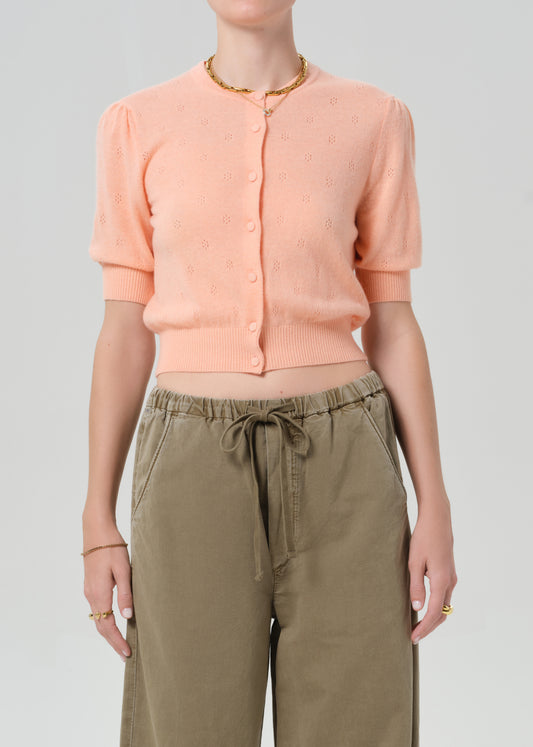 Person wearing a peach cardigan and brown pants on a gray background