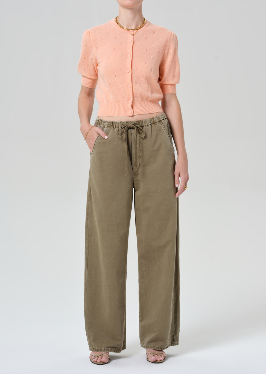 Person wearing a peach cardigan and olive green pants on a white background