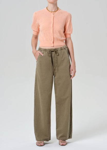 Person wearing a peach cardigan and olive green pants on a white background