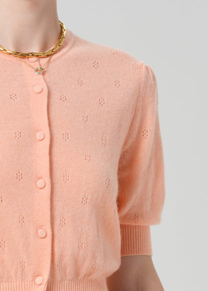 Close-up of a person wearing an orange cardigan with a subtle pattern on a plain background